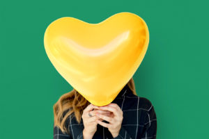 Woman with a heart balloon covering face