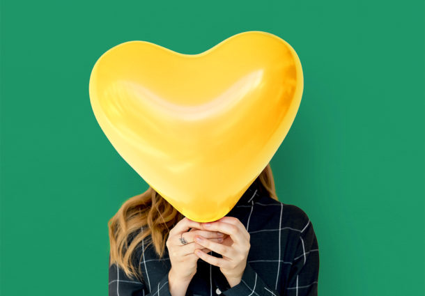 Woman with a heart balloon covering face