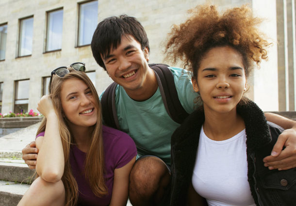 Three friends in embrace smile at the camera