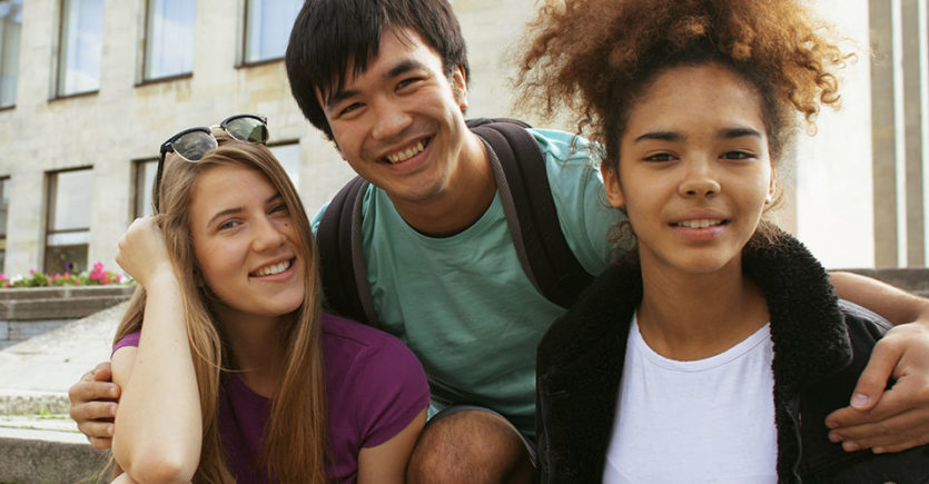 Three friends in embrace smile at the camera
