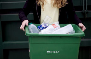 A woman holding a green recycling box bin