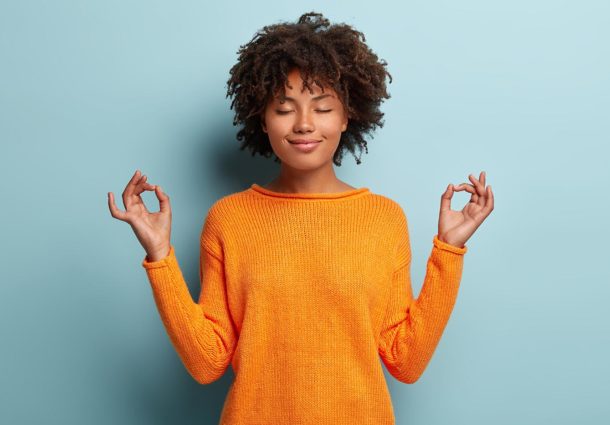 A woman stand with her eyes closed, and her hands in a meditation pose