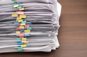 Image of a tall stack of documents held together with colourful bulldog clips