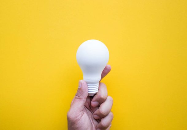 A hand holding a single lightbulb on a yellow background