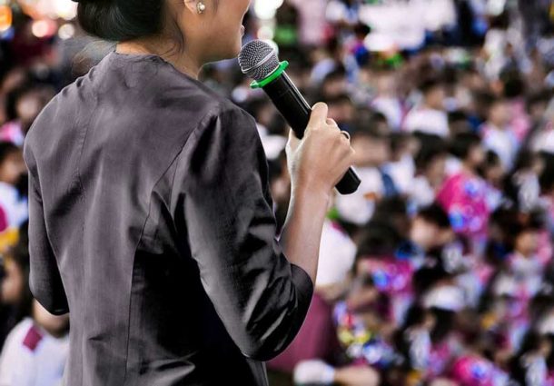 A woman with a microphone addresses an audience