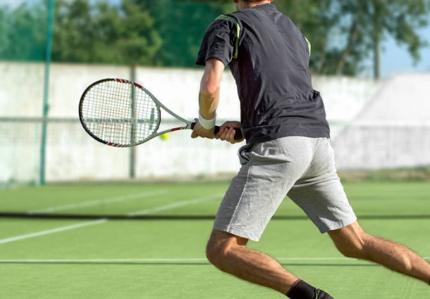A man running across a tennis court ready to swing