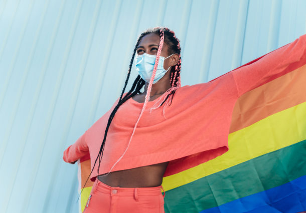 Person of colour with an LGBTQ+ flag and mask